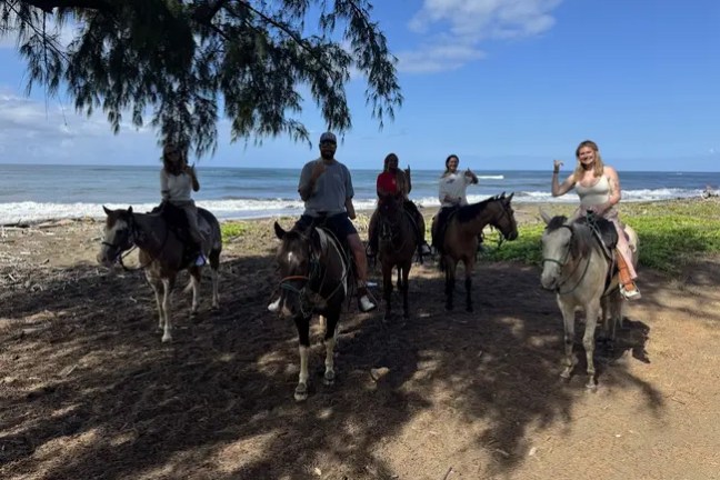 Five people on horseback near the beach with ocean in the background.