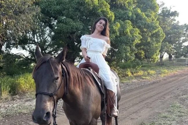 Woman in white dress riding a horse on a dirt path.